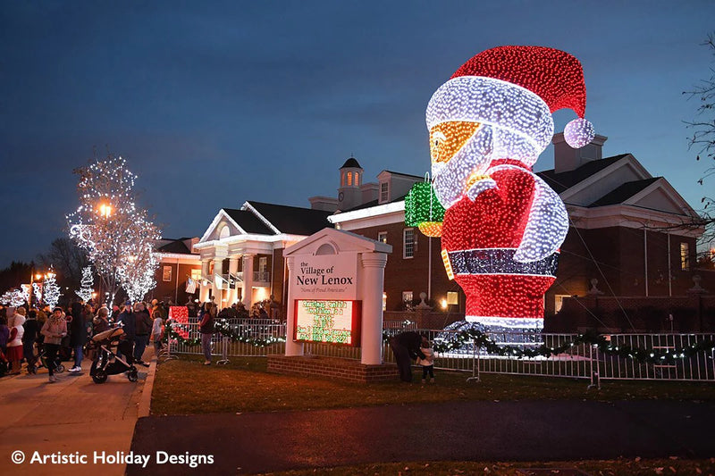 Decorative light display of a giant Santa Claus figure in front of a building with holiday lights.